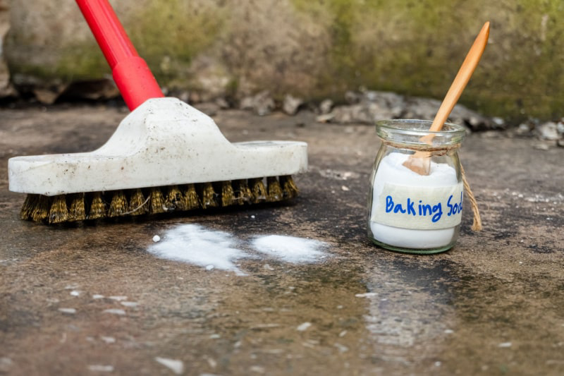 Person using wire brush and baking soda to remove grease stain on driveway