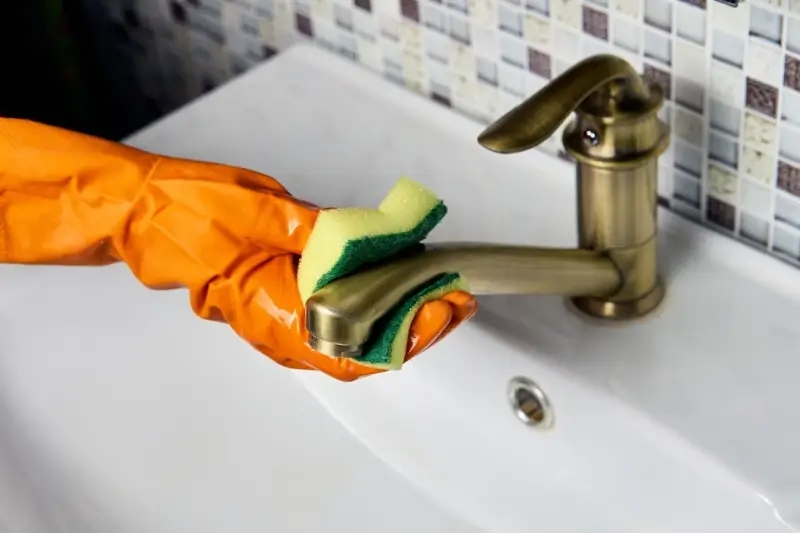 Cleaner wiping brass sink faucet with a sponge.