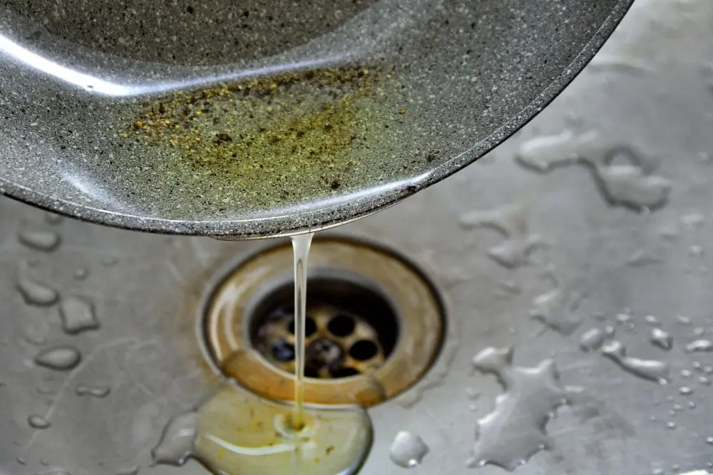 Person pouring oil from a pan down a garbage disposal.