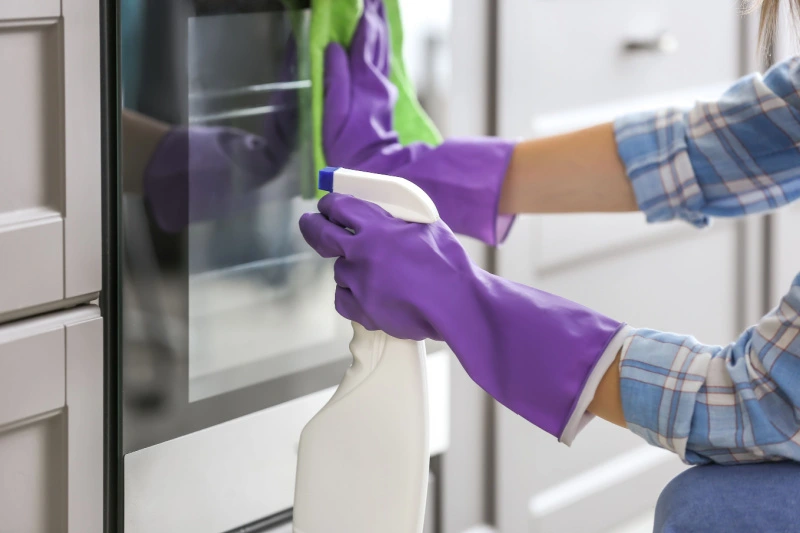 Person cleaning the outside of a glass oven door.