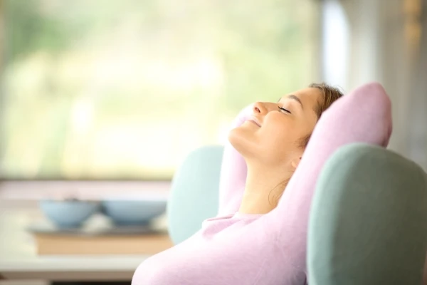 Woman with arms folded behind her head and eyes closed relaxing on her couch at home.