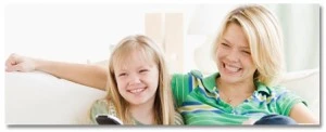 Mother and daughter sitting together on a white couch and smiling