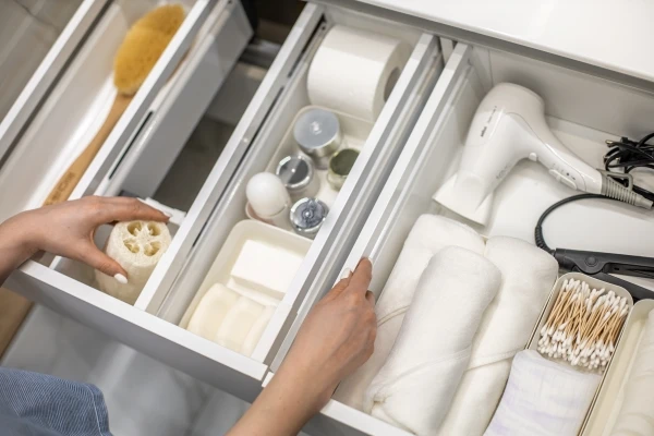 Top view of woman hands neatly organizing bathroom amenities and toiletries in bathroom drawer.