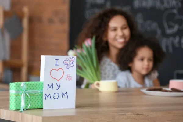 Greeting card and gift for Mother's Day on table in kitchen