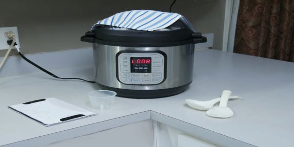 Instant pot sitting on white kitchen counter next to two white spoons.