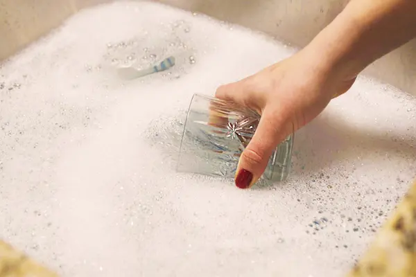 Close-up of manicured hand with red nail polish soaking crystal glass in tub of water.