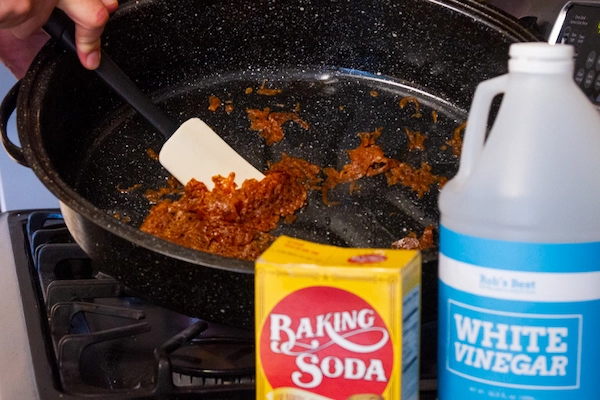 Close-up of roasted food being scraped off bottom of pan with rubber spatula.