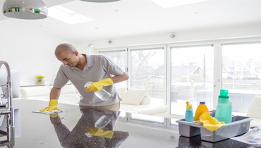 Young man cleaning a kitchen counter top with spray cleaner and cloth.