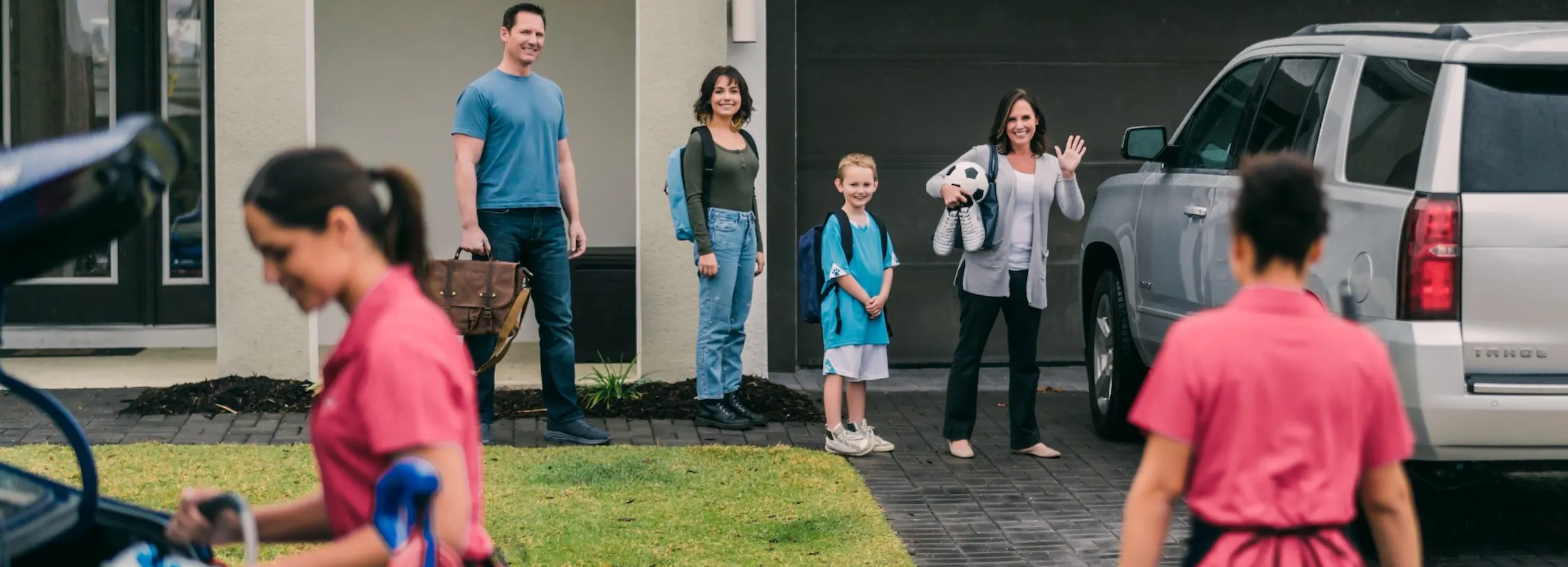 Family of four standing in driveway greeting pair of Molly Maid cleaning professionals arriving for residential service.