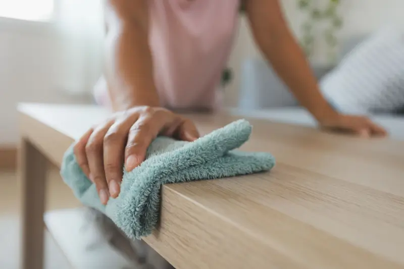 Person wiping coffee table in living room